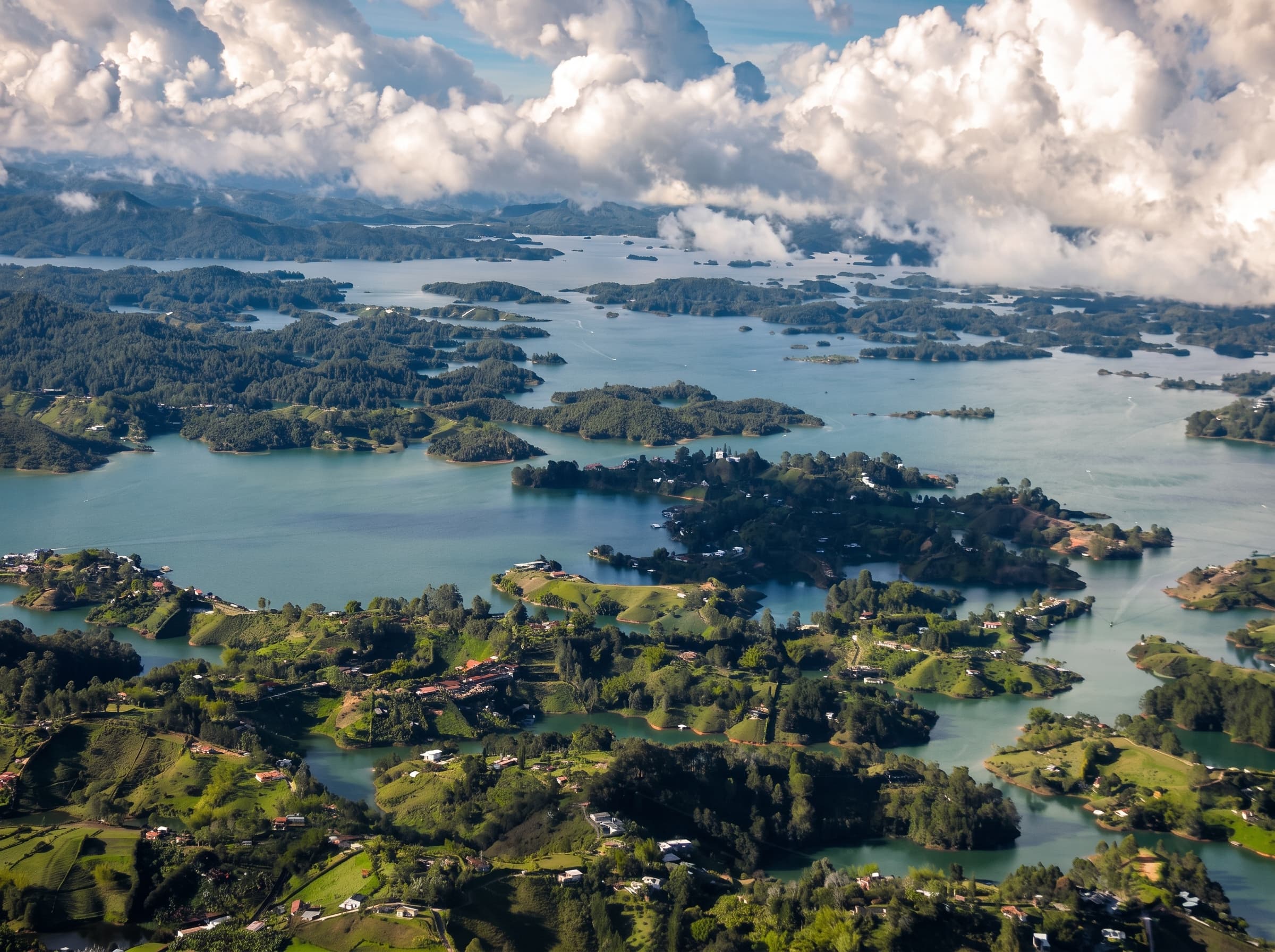 Vista aérea de un embalse colombiano con islas verdes entre montañas y nubes